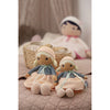 Two dolls sitting on a bed, with a basket and another doll in the background.